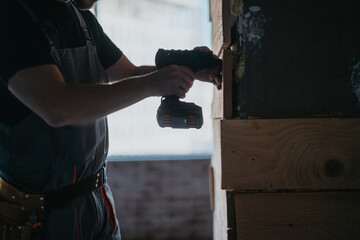 A person working on a wooden fixture using a power drill during a construction project, emphasizing...