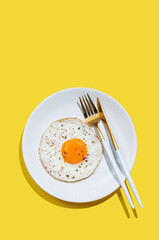 Fried eggs with spicy and cutlery on a white plate on a bright yellow background with shadow.