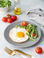 Fried eggs with arugula and cherry tomatoes on a dark plate on a blue txtured background