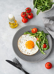 Fried eggs with arugula and cherry tomatoes on a dark plate on a blue txtured background