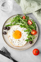 Fried eggs with arugula, ovives  and cherry tomatoes on a plate on a light background