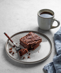 Chocolate brownie on a plate on a light background with cup of freshly brewed coffee and napkin.