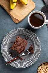 Vegetarian chocolate banana brownie on a plate on a dark background with a cup of coffee