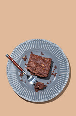 Chocolate brownie on a dark plate with a fork on a brown background with a bright shadow.