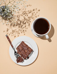 Chocolate brownie on a plate on a beige background with cup of freshly brewed coffee