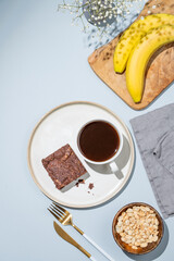 Chocolate banana brownie on a plate on a blue background with a cup of coffee, nuts and fresh fruits.