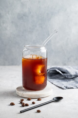 Cold brew coffee in a glass with ice on a light background with coffee beans and spoon.