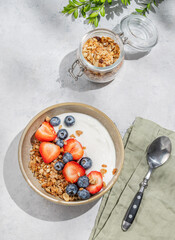Natural yogurt with granola, blueberry and strawberry in a bowlon a light background