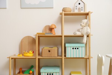 Shelving unit with decor and toys near white wall in stylish playroom. Interior design
