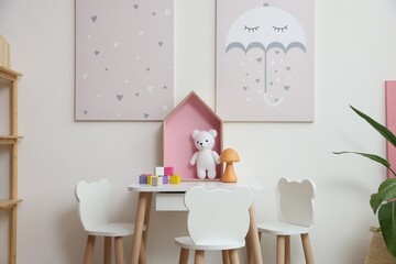 Small table, chairs and decor near white wall in stylish playroom. Interior design