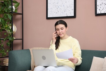 Young woman with laptop and papers complaining to someone via phone at home