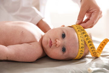 Pediatrician measuring baby's head with tape at table in clinic, closeup