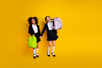 Smiling classmates holding backpacks, jumping on a yellow background, symbolizing friendship,...