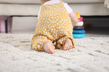 Cute little baby playing with toy pyramid on floor at home, back view