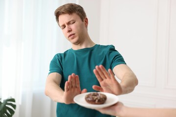 Gluten free diet. Man refusing from donut indoors, selective focus