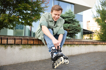 Happy young man putting on roller skates outdoors