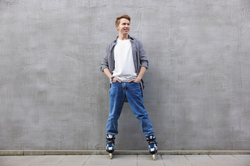 Happy young man with roller skates near gray wall outdoors
