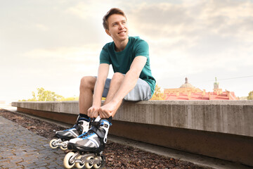 Happy man putting on roller skates outdoors