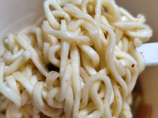 Rolls of springy white instant noodles are lifted with a fork from the bowl, highlighting their...