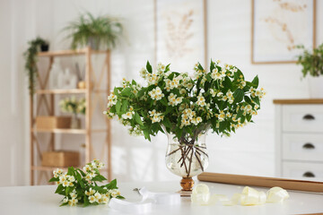Bouquet of beautiful jasmine flowers in vase on white table indoors