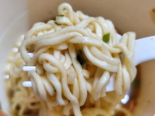Rolls of springy white instant noodles are lifted with a fork from the bowl, highlighting their...