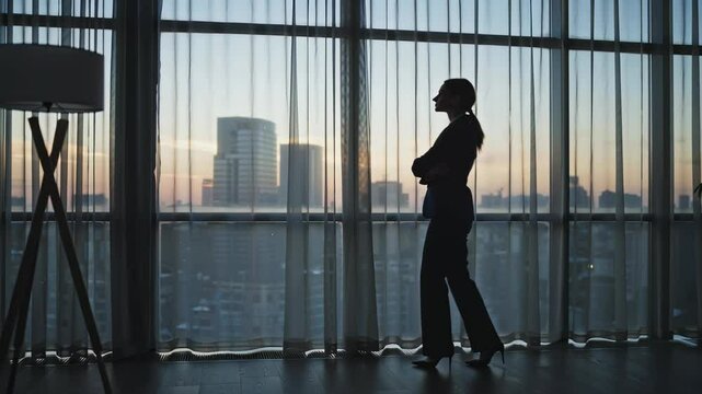 Businesswoman standing in silhouette by window, looking out at city skyline with soft curtain backdrop. Evening light creates serene atmosphere. Concept of business, motivation, urban lifestyle - Powered by Adobe