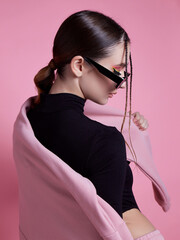 A woman in a pink hoodie and sweatpants poses for a photo. The pink color of her outfit gives off a...
