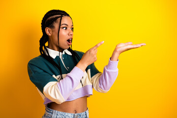 Young fashionable woman with braided hair showing with hand against vibrant yellow background,...