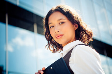 Confident young businesswoman standing outdoors near modern glass office building during daylight