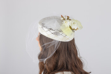 Elegant wedding hat worn by a young girl, seen from behind, set against a smooth grey studio...