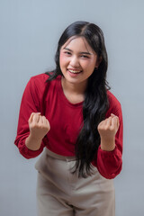 Cheerful young Indonesian woman leaning forward with both fists clenched in a playful victory pose....