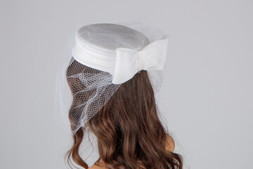 Elegant wedding hat worn by a young girl, seen from behind, set against a smooth grey studio...