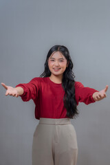 Young Indonesian woman with long black hair, smiling and gesturing with outstretched arms. Wearing...
