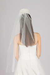 Elegant bridal veil on a young girl, seen from behind, against a soft grey studio backdrop
