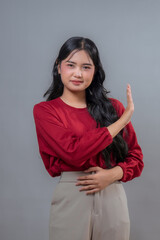 Young Indonesian woman wearing a red top and beige pants, raising her hand in a “stop” gesture...