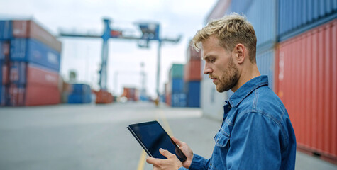 Engineer using digital tablet at shipping container yard for logistics management and inventory control.