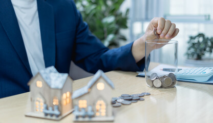 Close-up of hand placing coins into a jar, symbolizing saving money for real estate investment, financial planning, property purchase, or long-term wealth accumulation goals.
