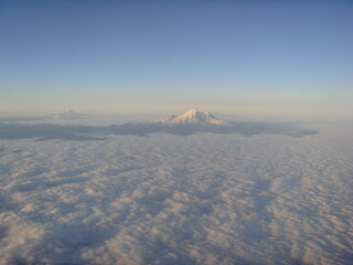 Aerial view of snow-capped mountains above cloud blanket at sunrise