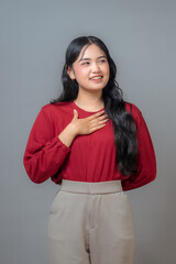 An Indonesian woman in a red shirt and beige pants, smiling warmly while placing her hand on her...