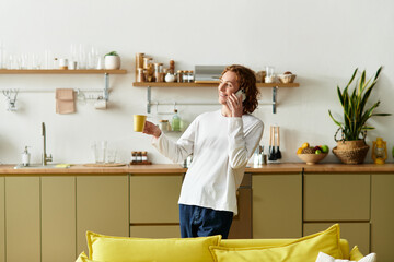 Young man enjoying a relaxed moment at home while talking on the phone and sipping tea