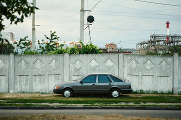 Old grey car under white fence in city