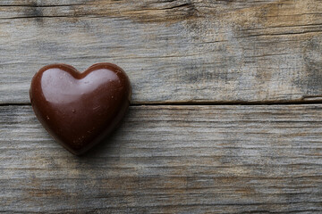 A close-up of various heart-shaped chocolates, including dark, milk, and white, with different toppings, arranged on a rustic wooden surface.