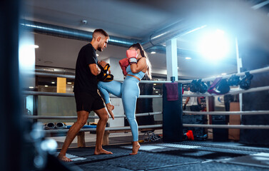 Female kickboxer training in boxing ring with male trainer at gym.
