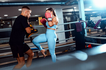 Female kickboxer training in boxing ring with male trainer at gym.