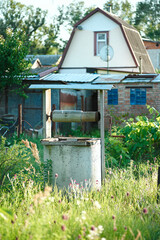 Old concrete well in the middle of green grass against the background of an old house