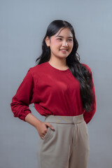Confident young Indonesian woman in a red long-sleeve top and beige trousers, standing with one...