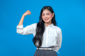 Smiling young Asian woman in a white shirt and gray pants confidently showing a flexed arm muscle,...