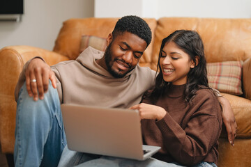 Couple sharing a joyful moment while browsing on a laptop in a cozy living room during a relaxed...