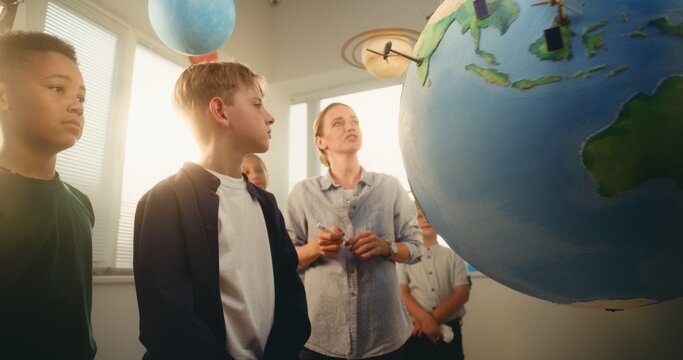 STEM Science Lesson: Female Teacher Educating Smart Diverse Kids Using Globe with Miniature 3D Models of Wind Turbines and Solar Panels. Primary School Children Studying Renewable Energy and Ecology.