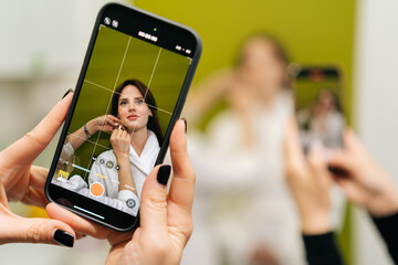 Professional beautician applying makeup while female hands recording process, creating social media beauty tutorial with smartphone in modern beauty clinic. Concept of anti-age rejuvenation skincare.